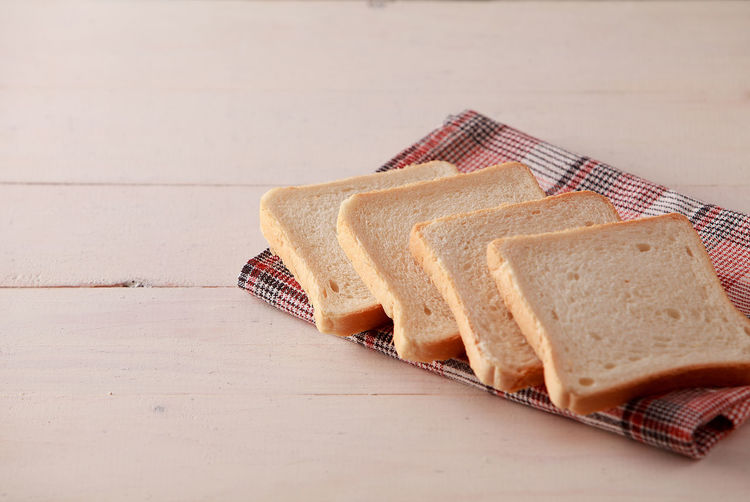 A stack of sliced bread toasts on white wooden background