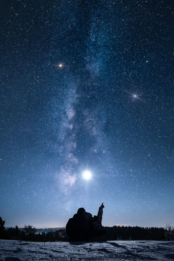 Silhouette couple sitting on mountain against star field at night