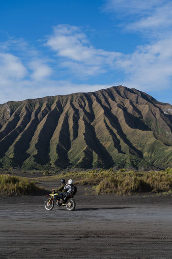 A motorbikewith two people driving in an amazing landscape with green hills as the background