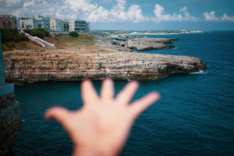 Cropped image of hand on rock by sea against sky