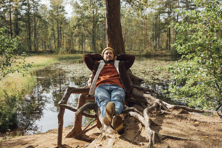 Man with eyes closed relaxing near tree in forest
