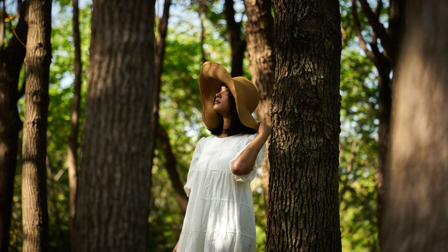 Woman standing by tree trunk in forest