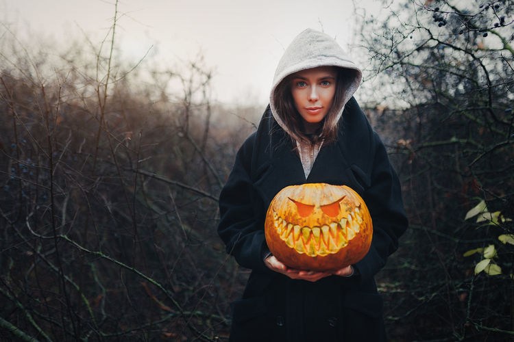 Portrait of woman holding pumpkin in forest during autumn