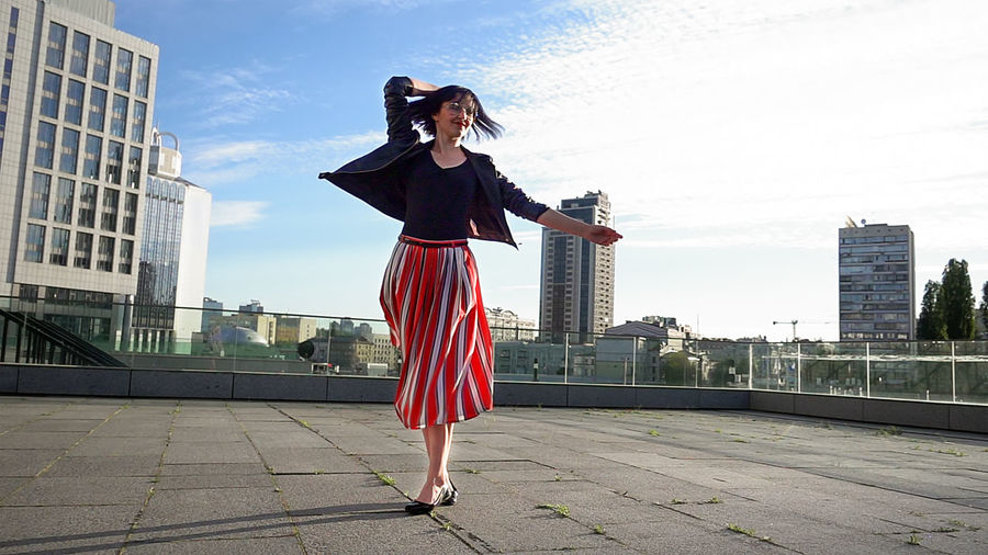 Happy woman wearing striped skirt and jacket on footpath in city
