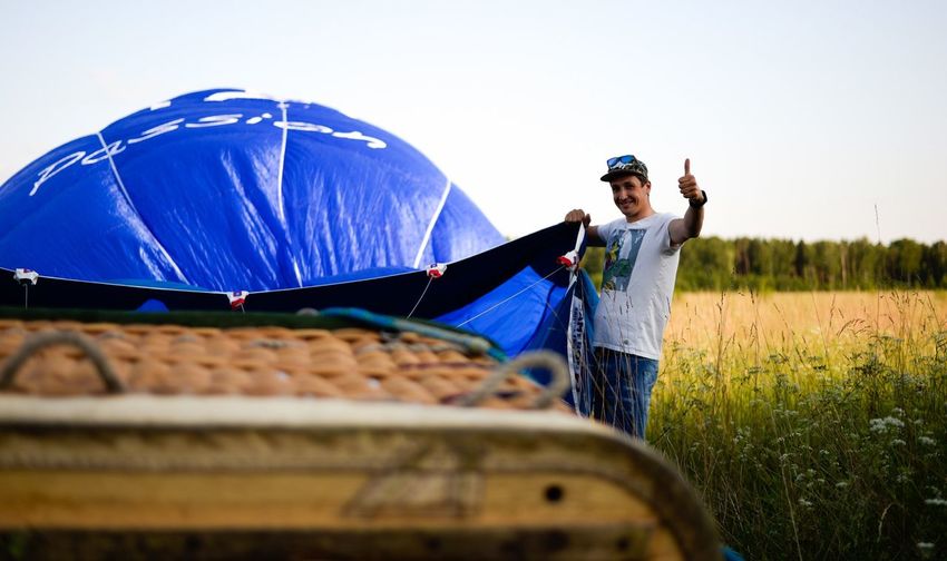 Portrait of man showing thumbs up while putting up tent on field