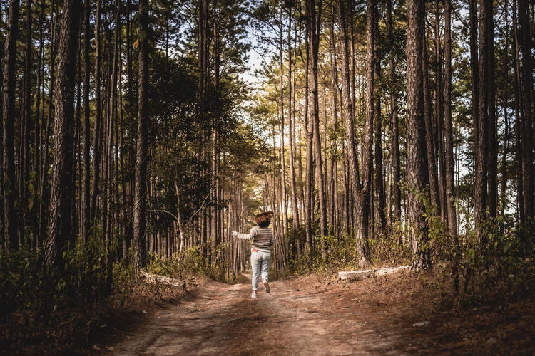 Rear view of woman running on dirt road amidst trees in forest