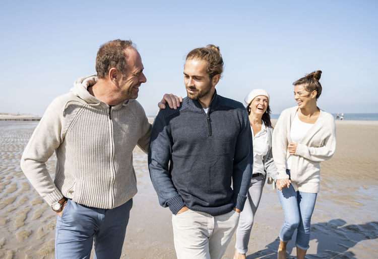 Men talking while walking with women in background at beach