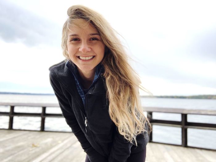 Portrait of young woman smiling while standing on pier over sea against sky