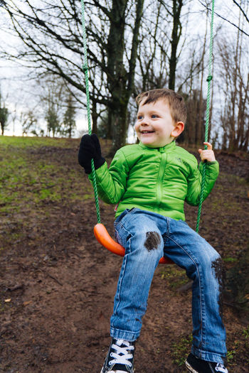 Portrait of boy standing on swing at park