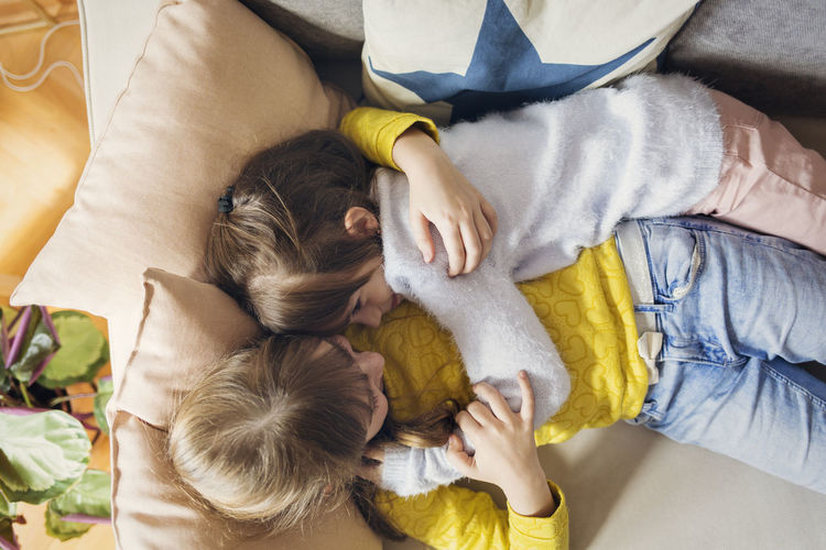 Overhead view of sisters embracing while relaxing on sofa at home