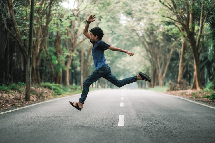 A boy jumping in the middle of an empty road in the countryside