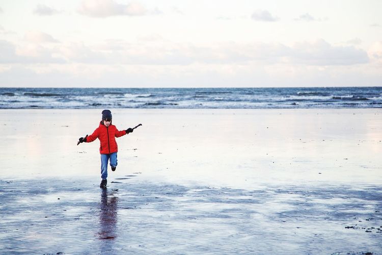 Boy running on beach against sky