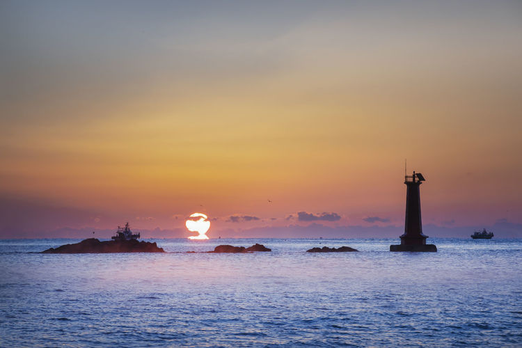 Lighthouse by sea against sky during sunset