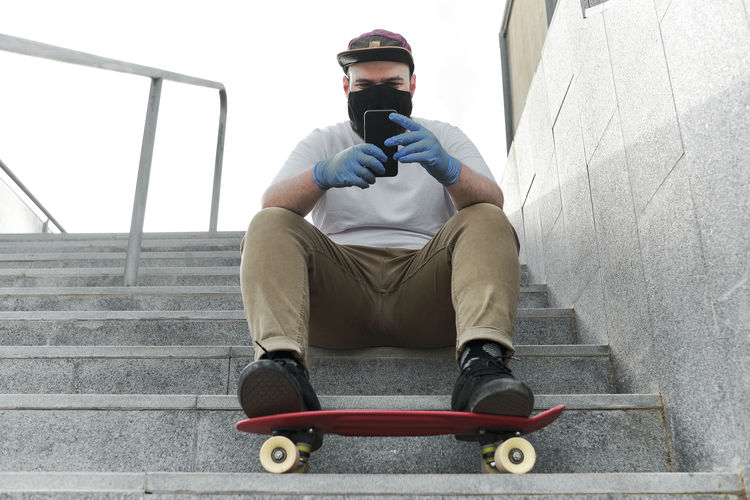 Young man looking at smartphone with red skateboard , blue gloves and mask
