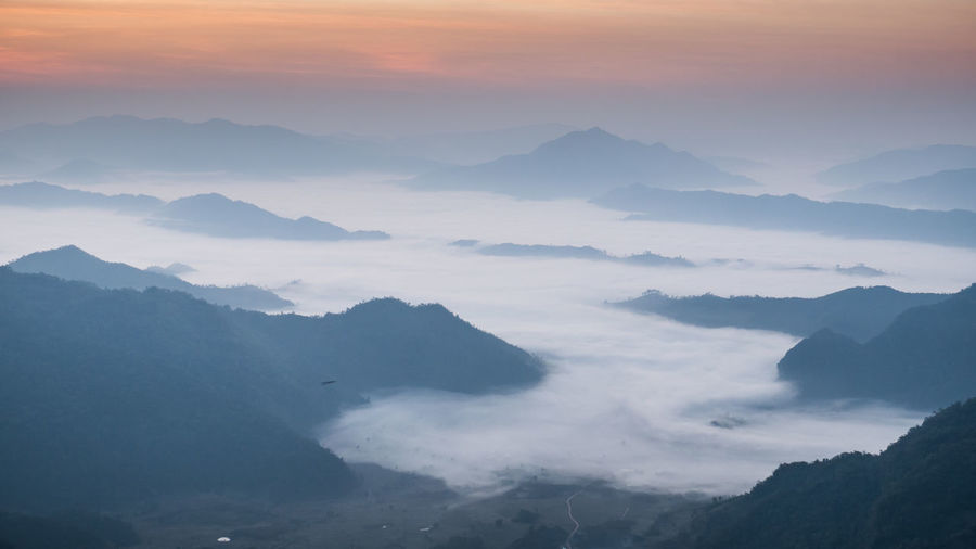 Scenic view of silhouette mountains in foggy weather during sunrise