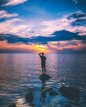 Rear view of man standing on rock against sea during sunset