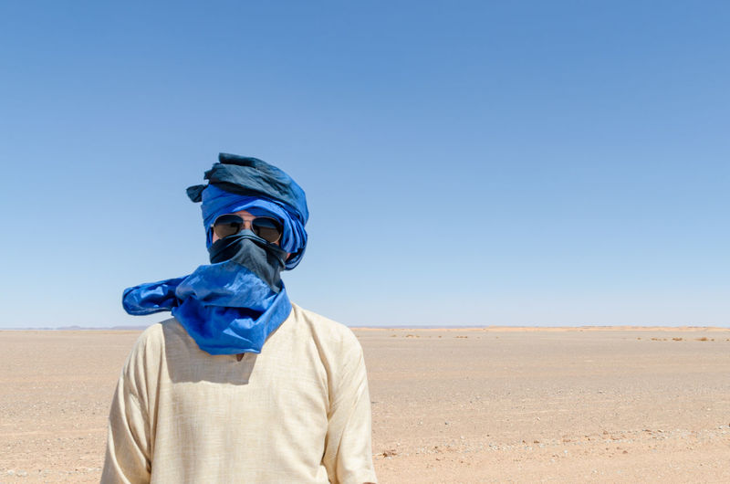 Man with headscarf standing in desert against clear blue sky