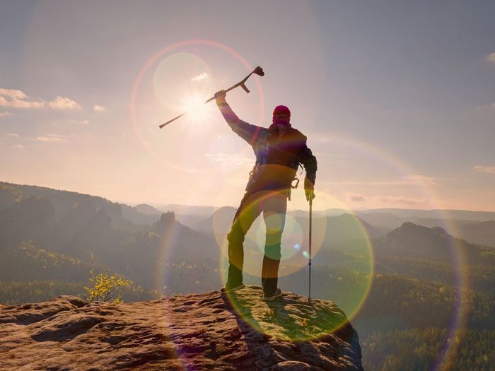 Rear view of man with arms outstretched standing on mountain against sky during sunset