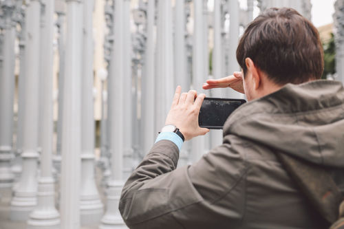 Rear view of man photographing columns of urban lights on smart phone