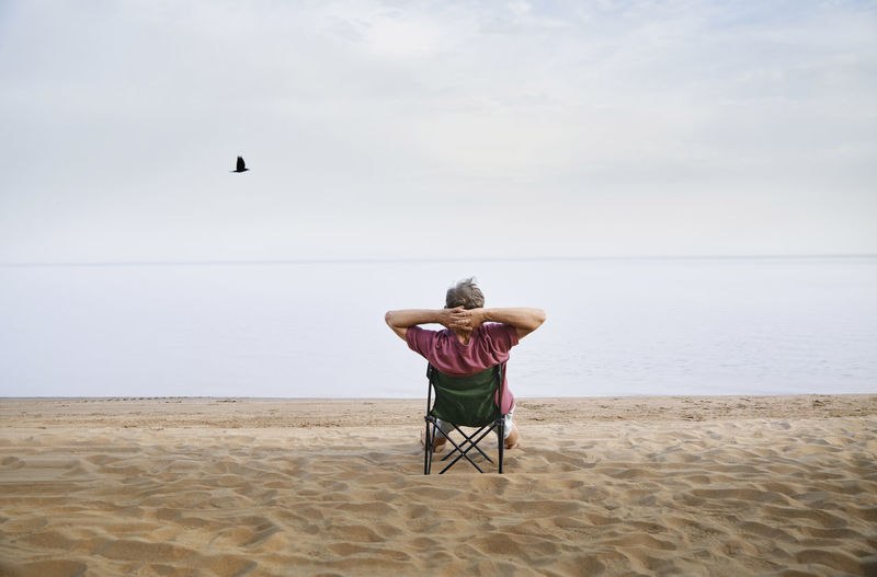 Senior man sitting on folding chair relaxing at beach