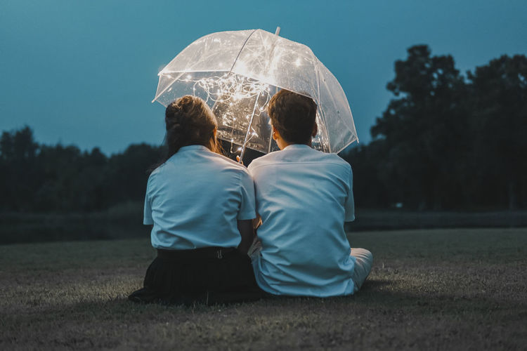Rear view of couple sitting with umbrella on land at night
