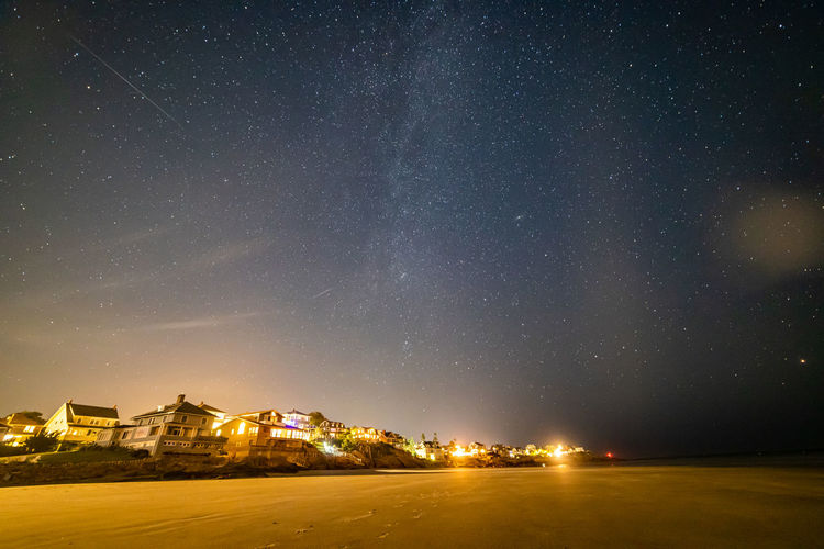 Meteors and the milky way galaxy in the night sky above beach houses.