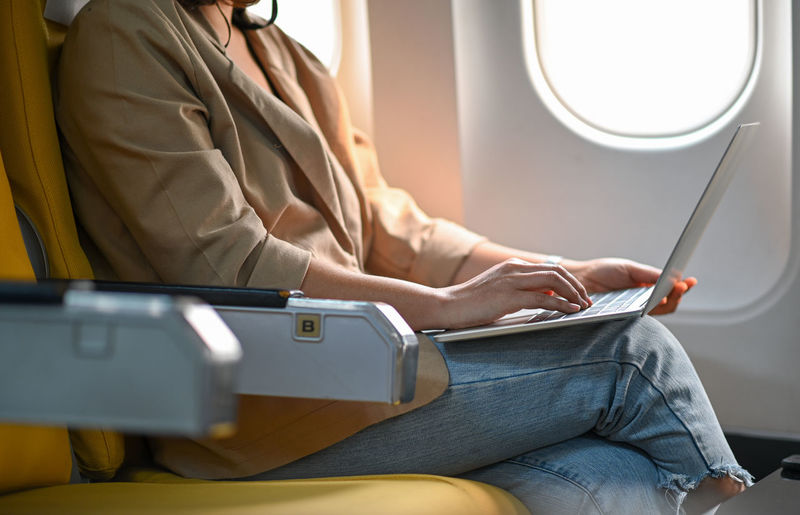 Midsection of woman using laptop in airplane