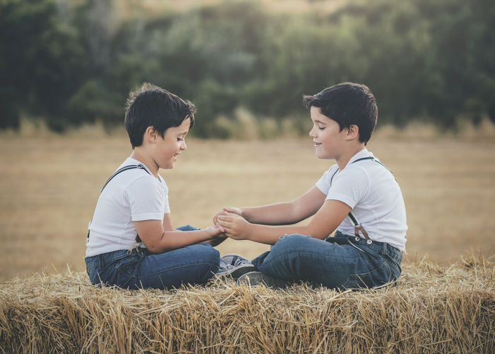 Side view of boys sitting on hay bale