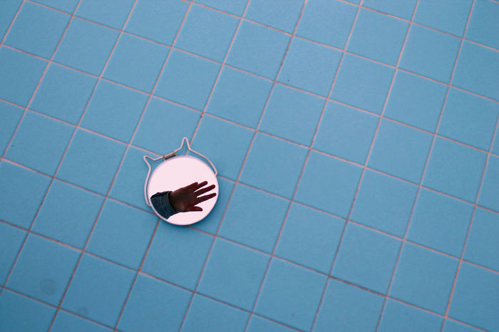 High angle view of hand reflection on mirror over blue tiled floor