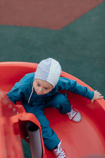 Cute little boy with down syndrome in hat walks in the playground, rolling down the children's slide