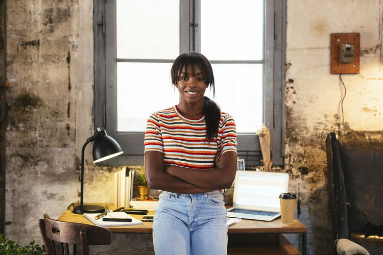 Portrait of smiling young woman standing front of desk in a loft