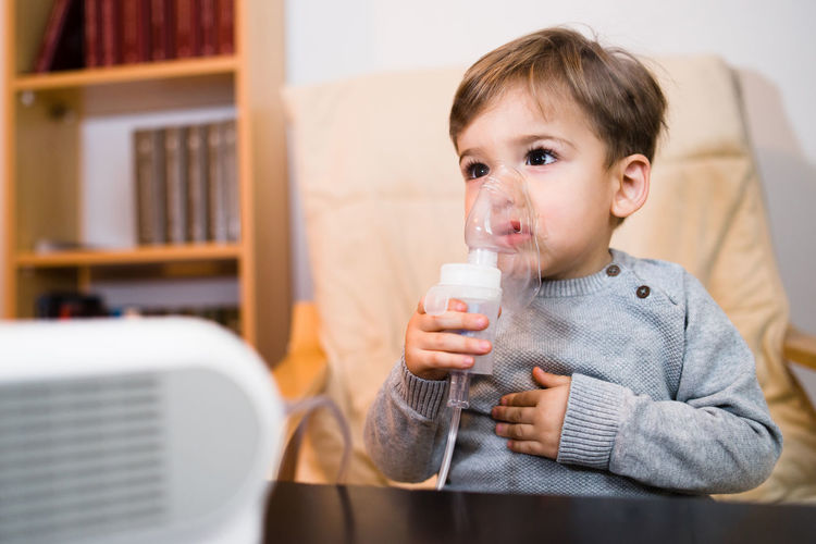 Boy looking away while inhaling through respiratory mask at home