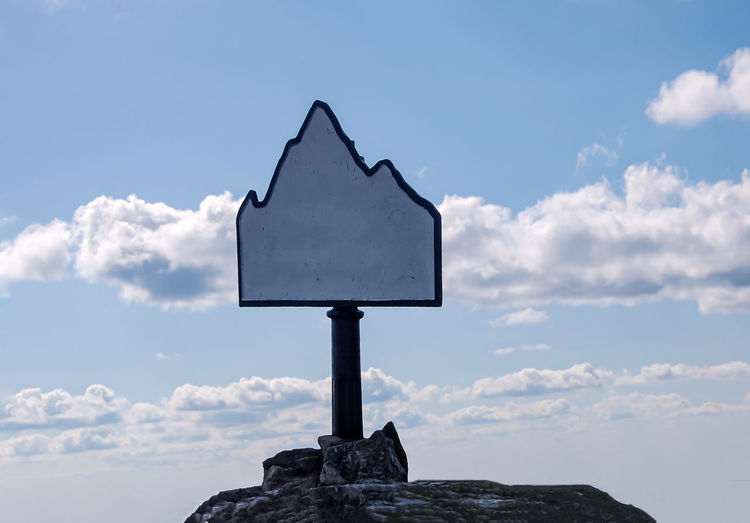 Low angle view of sign on rock against sky