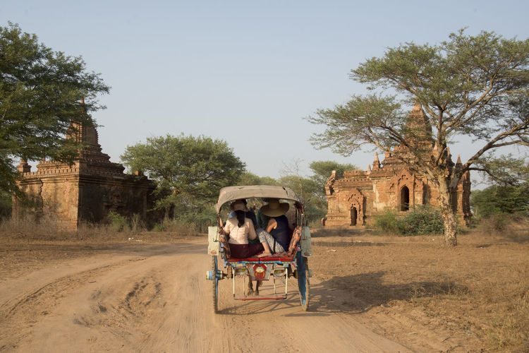 People traveling from cart on dirt road against temple