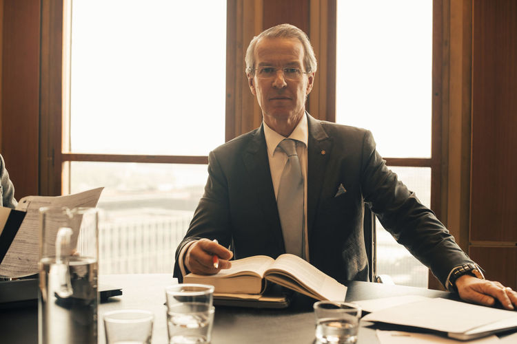 Portrait of confident mature lawyer with book at conference table in office
