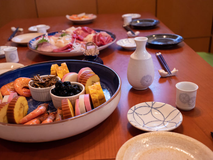 The table being set for a traditional new year's dinner in japan, with sashimi, osuimono and sake
