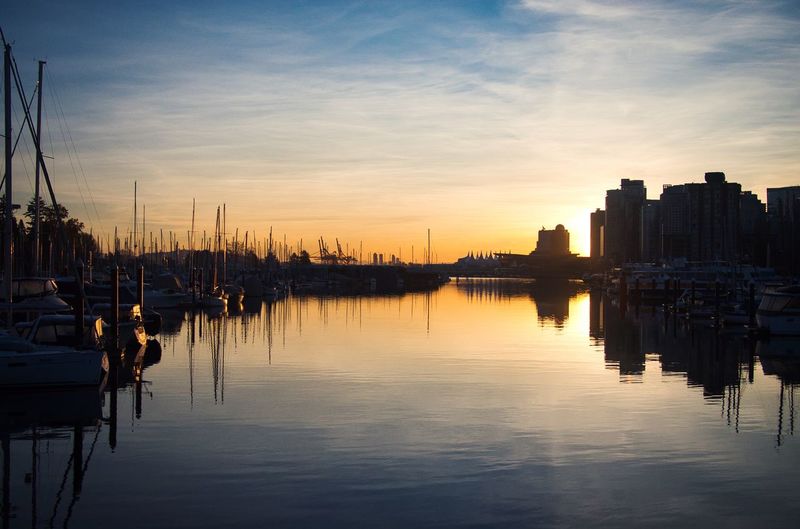 Sailboats moored in city during sunset
