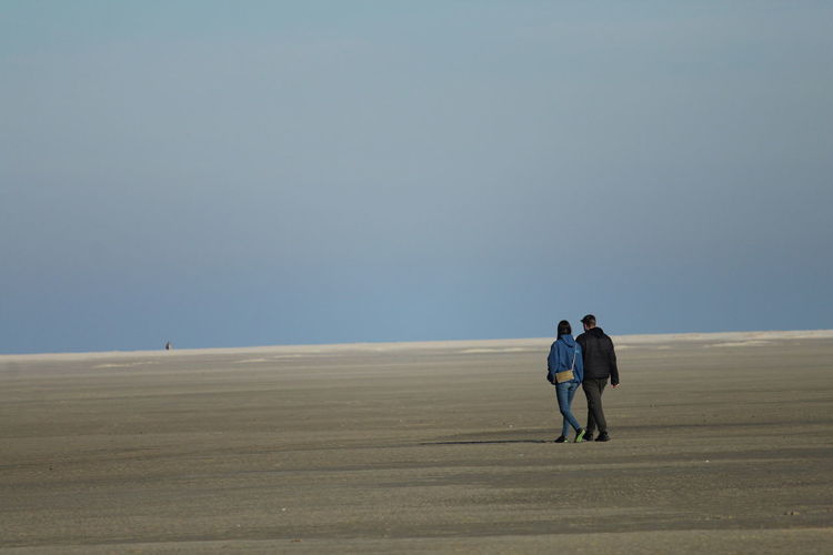 Rear view of man and woman walking on sand