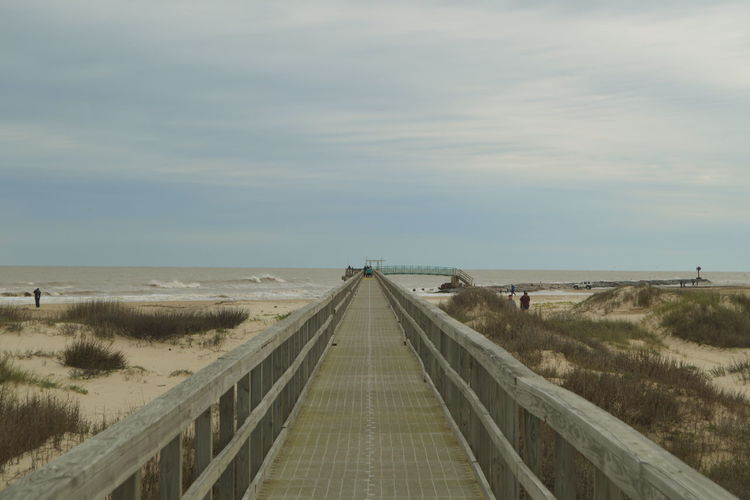 A walkway constructed of wood that leads out towards the ocean on the texas coast. 