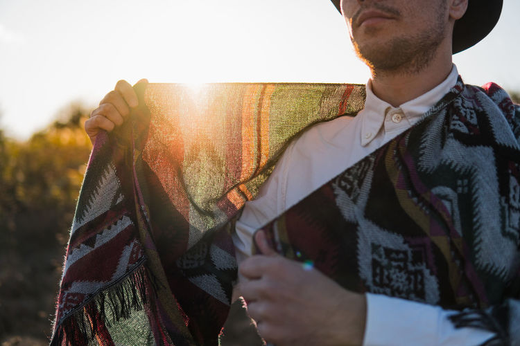 Man outdoors holds poncho against the sun, rural scene