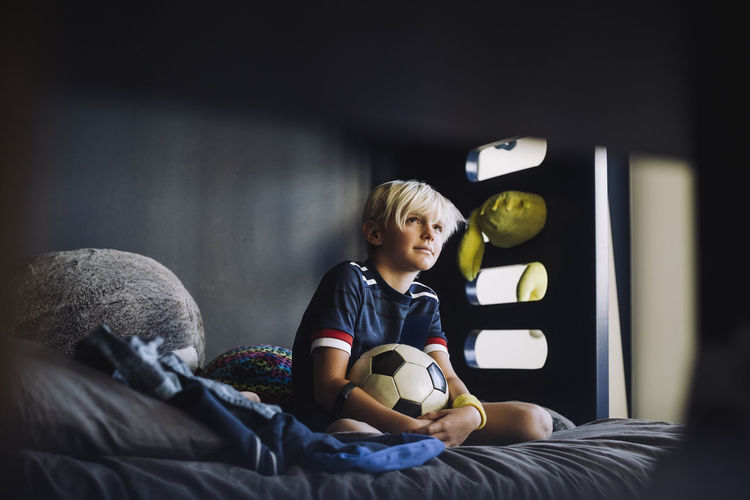Boy day dreaming while looking away in bedroom at home