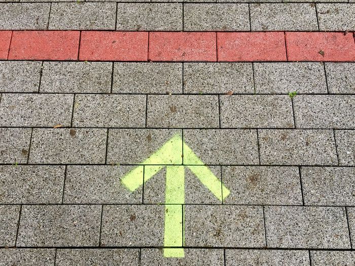 High angle view of yellow arrow symbol on footpath