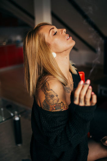 Young tattooed woman smoking and relaxing in her room.