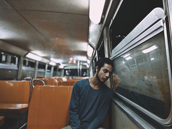 Thoughtful young man sitting by window while traveling in train