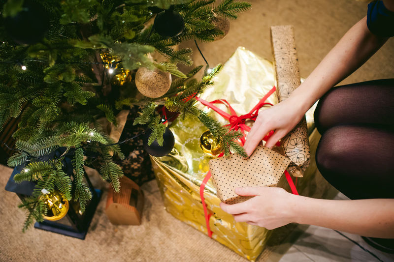 Midsection of woman with gift by christmas tree at home