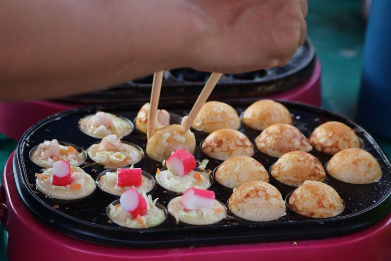 Cropped hand of person holding takoyaki with chopsticks