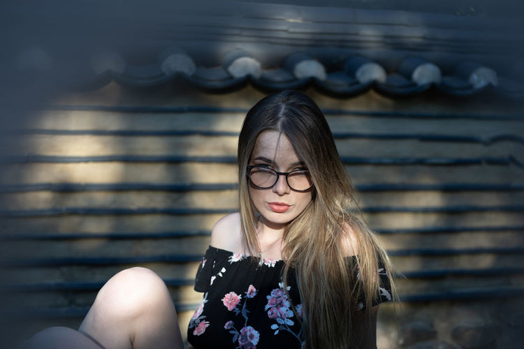 Portrait of beautiful young woman sitting by wall outdoors