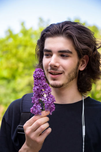 Portrait of a smiling young man holding purple flower
