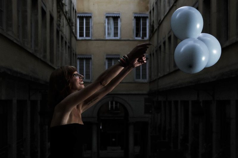 Woman holding balloons on building in city