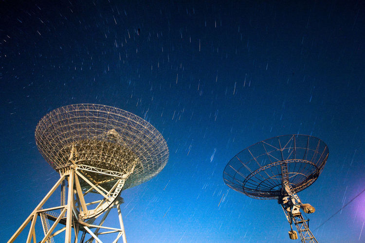 Low angle view of satellite dish against star trails at dusk
